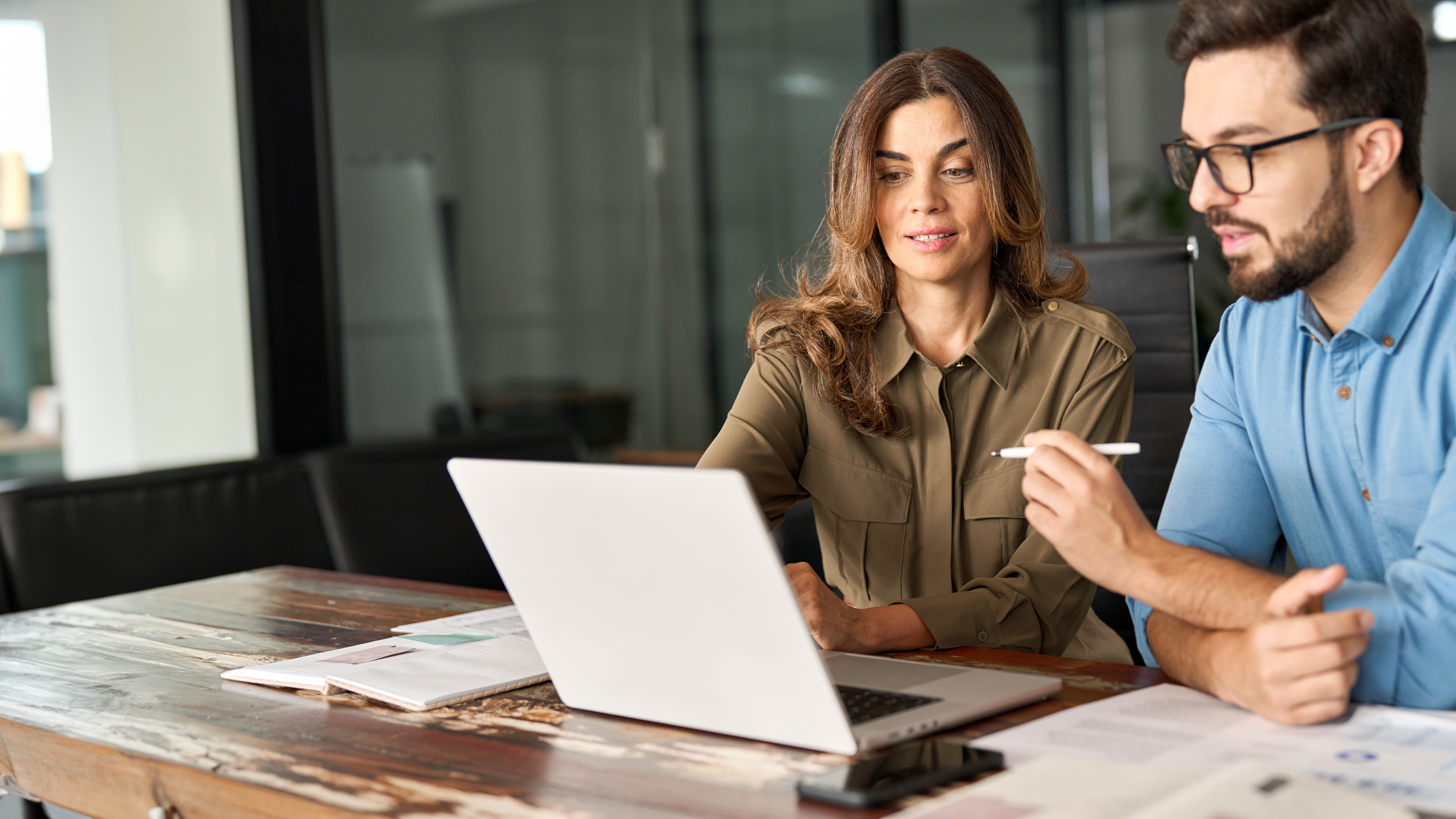 Businesswoman and businessman reviewing information on a laptop together at a rustic wooden desk